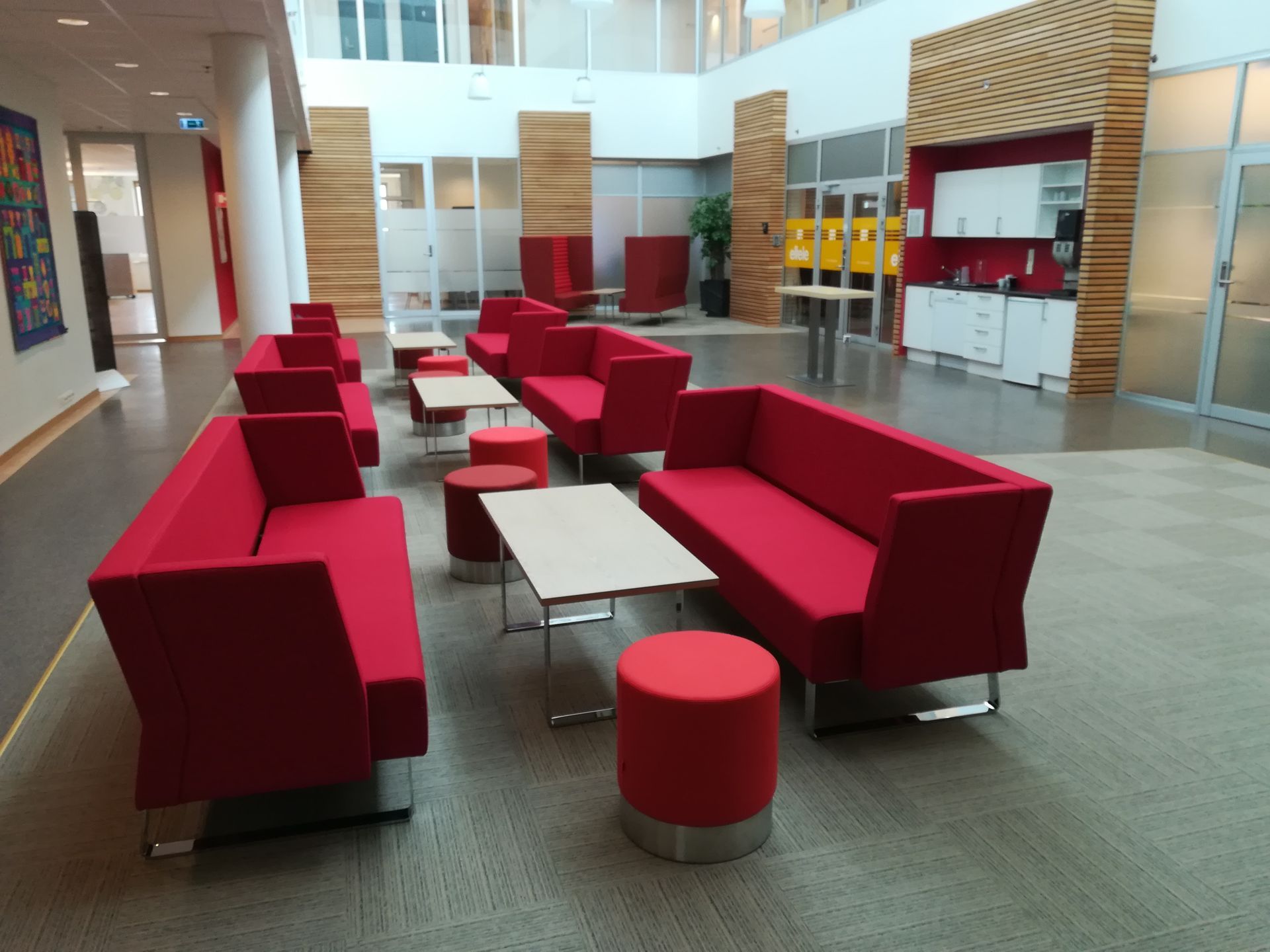 Røde sofaer og krakker i en moderne lobby med en lys trevegg.