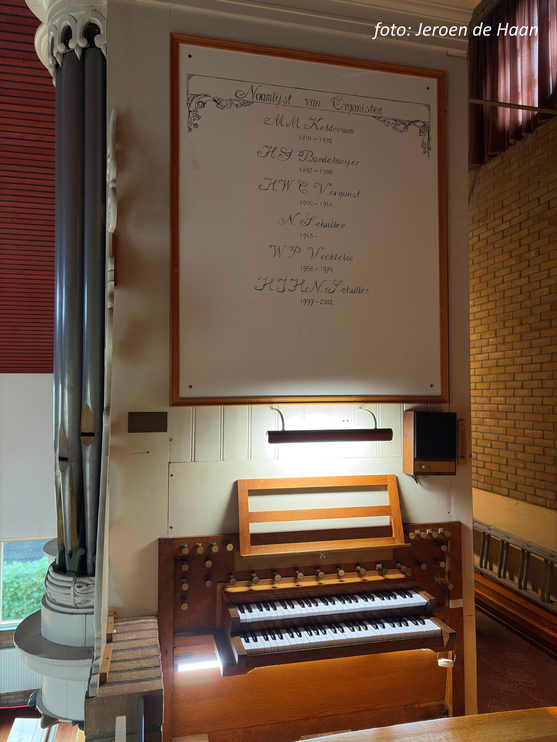 Een orgelconsole onder een ingelijst opschrift in een kerk.