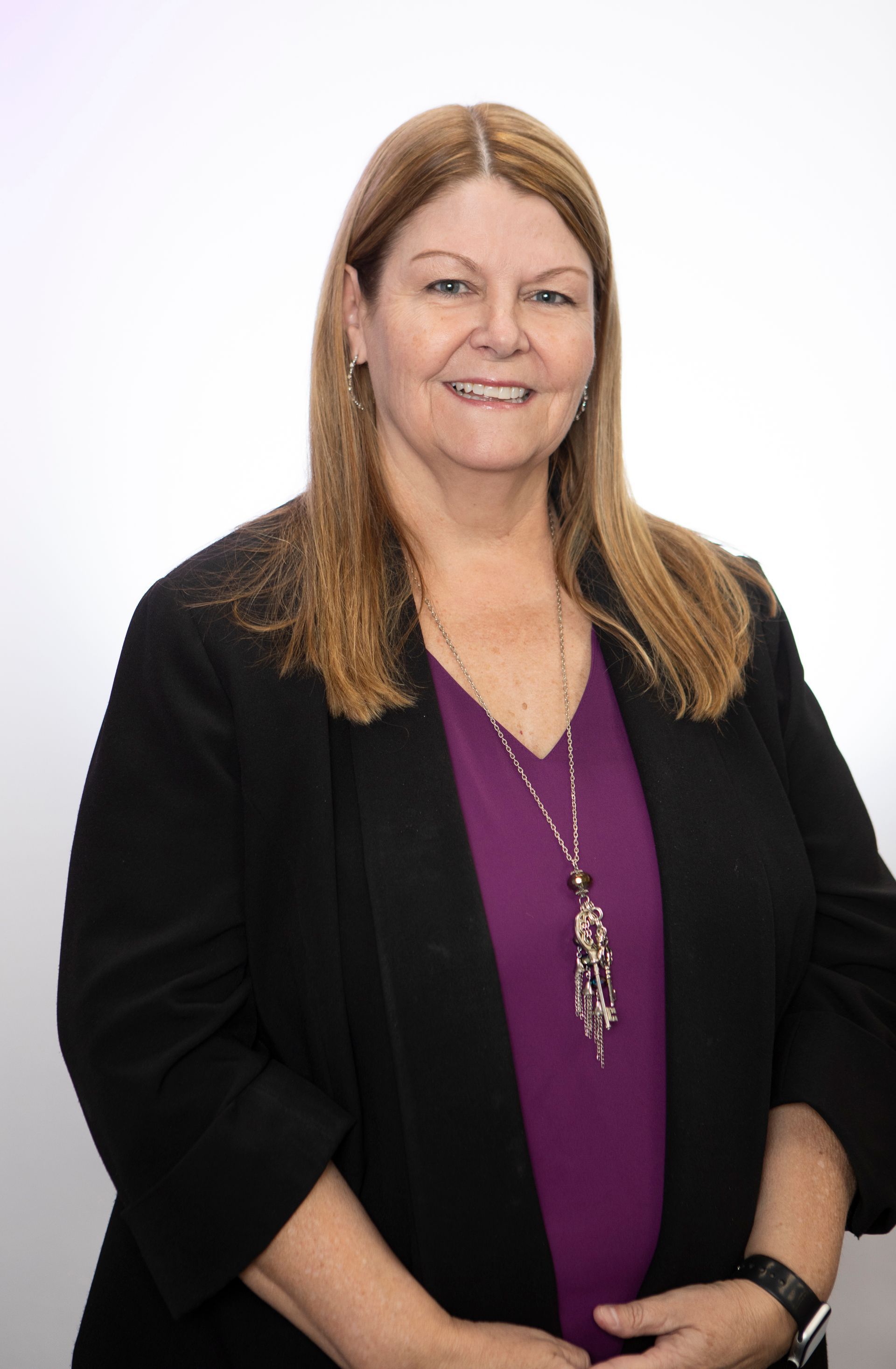 A woman wearing a black jacket and a purple shirt is smiling for the camera.