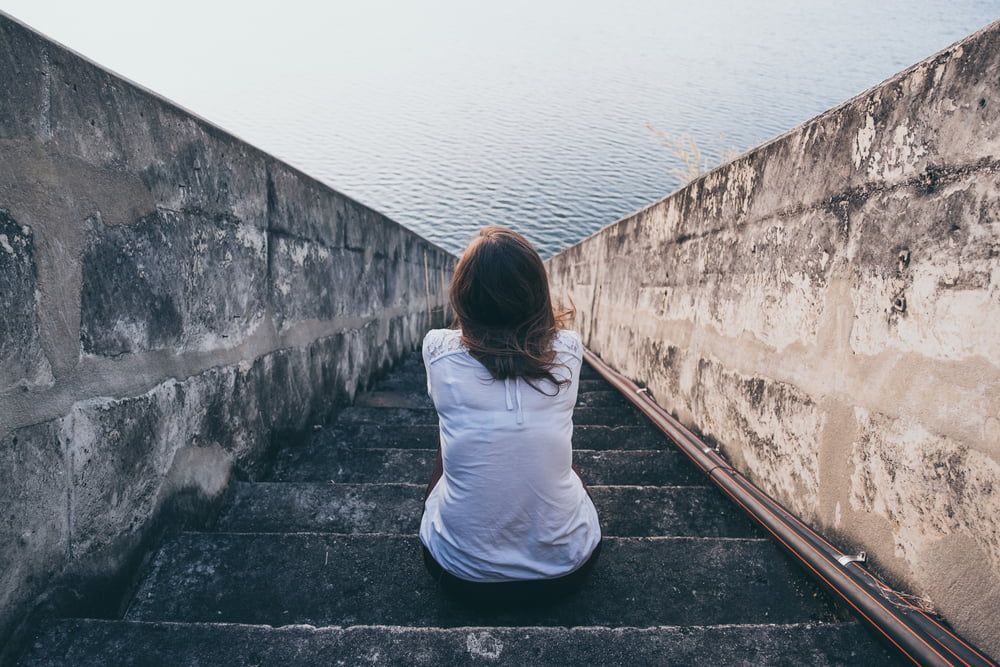 A depressed woman sits on a set of stairs looking at the water — Herbalism & Naturopathy on the Gold Coast QLD