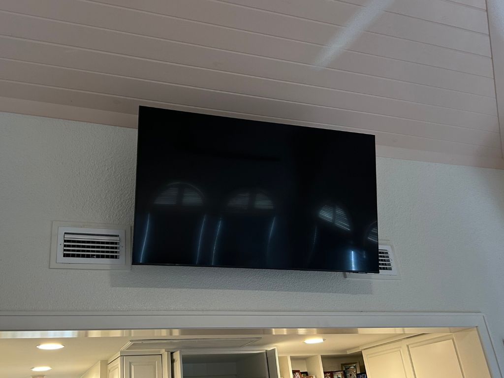 A flat screen tv is hanging from the ceiling in a kitchen.