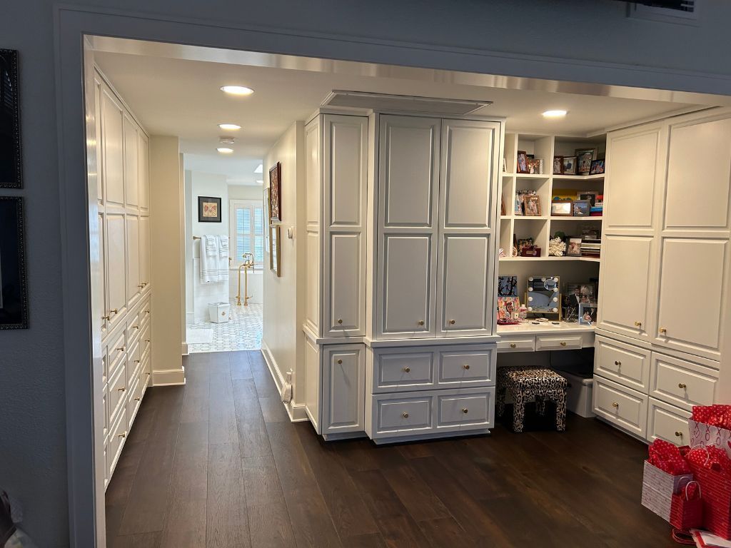 A room with lots of white cabinets and drawers and a desk.