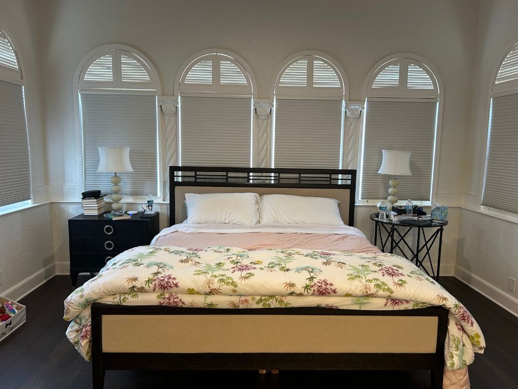 A bedroom with a bed , dresser , lamps and arched windows.