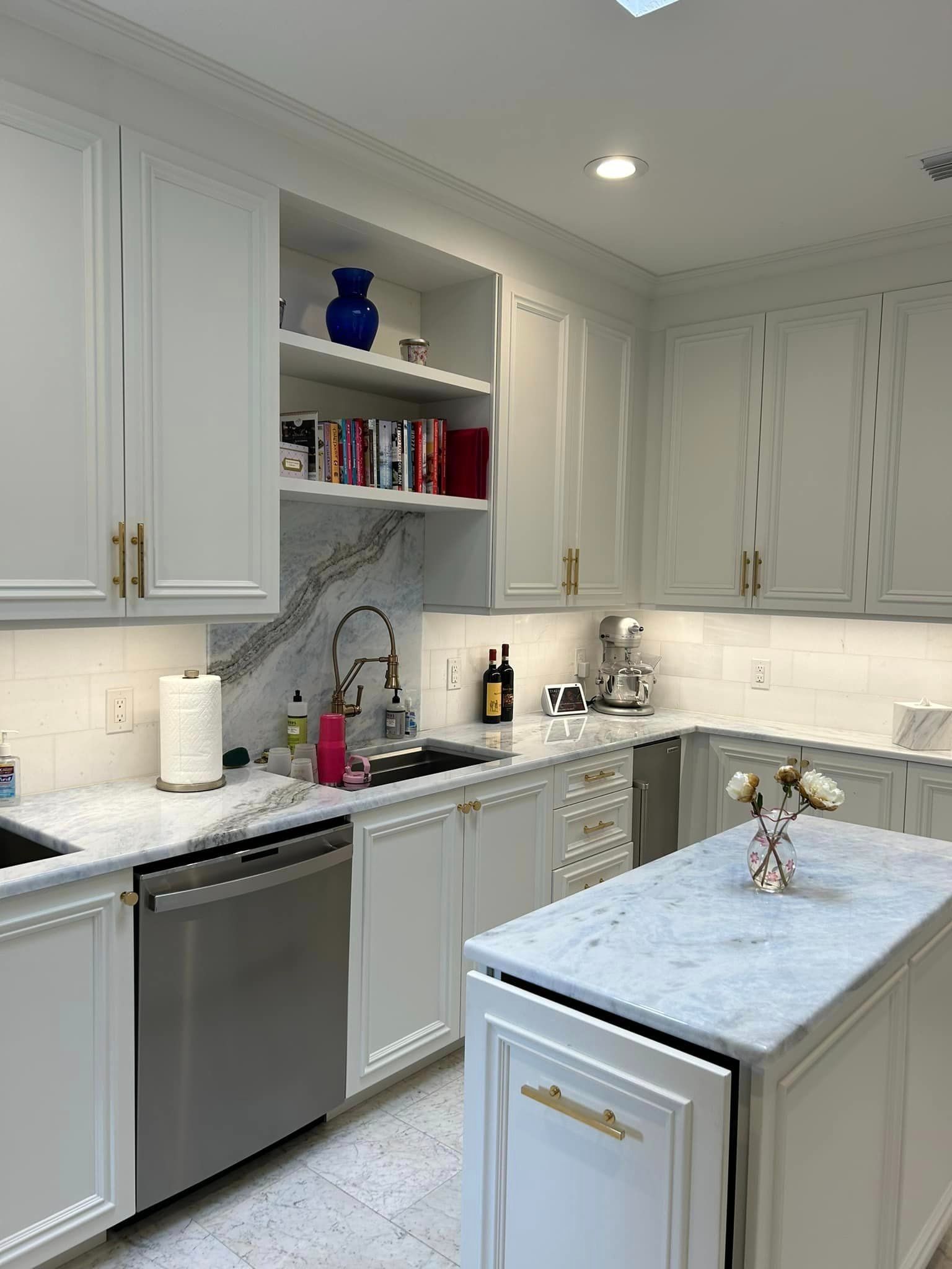 A kitchen with white cabinets , stainless steel appliances , a sink , and a large island.