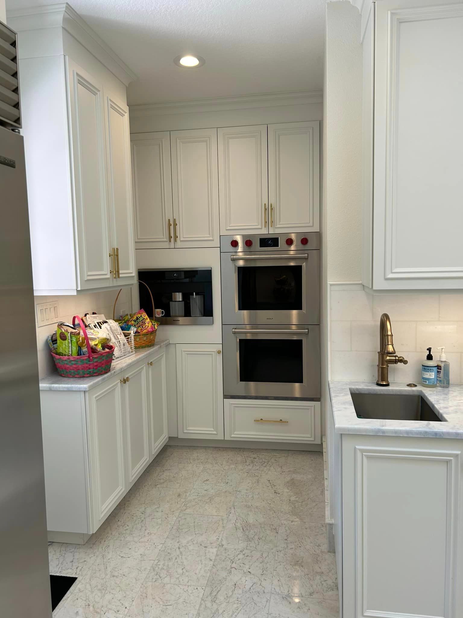 A kitchen with white cabinets , stainless steel appliances , a sink , and a double oven.