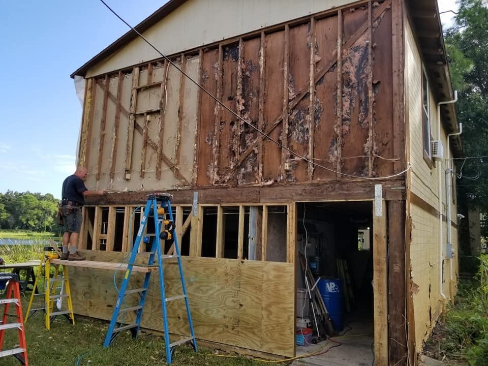 A man is standing on a ladder in front of a house that is being remodeled.