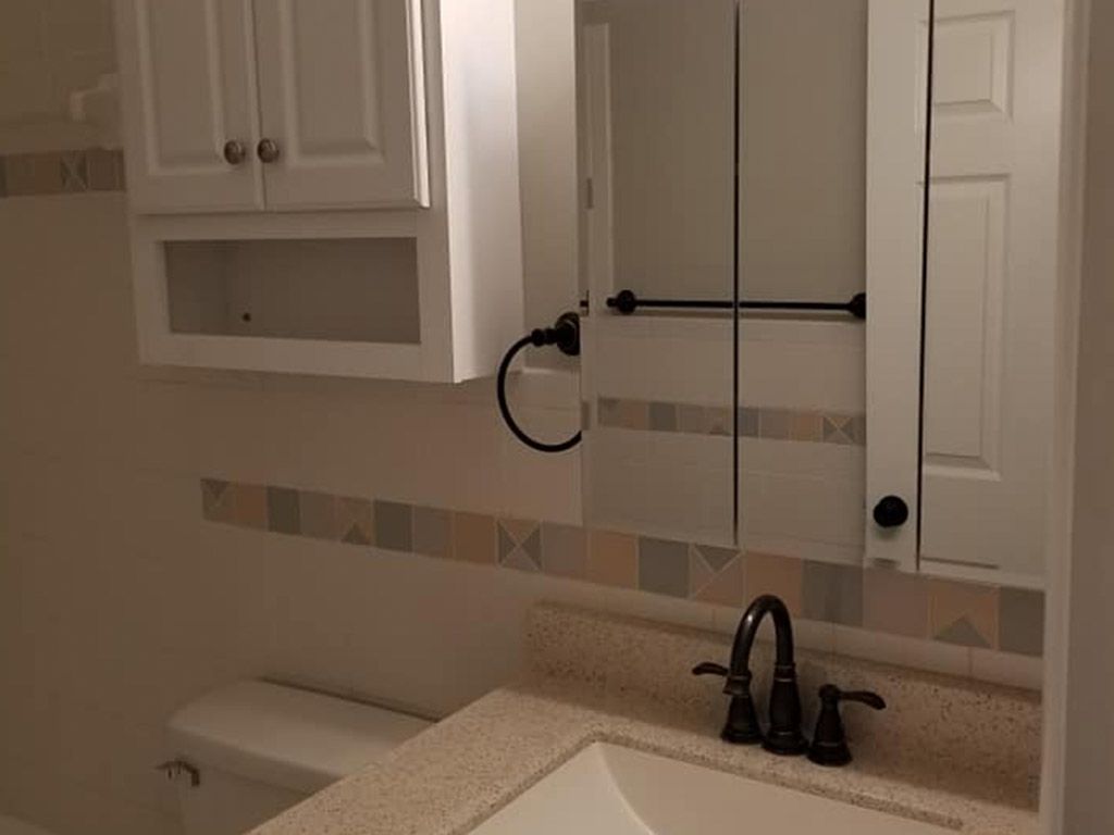 A bathroom with a sink , toilet , mirror and cabinets.