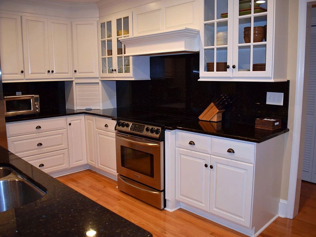 A kitchen with white cabinets and black counter tops