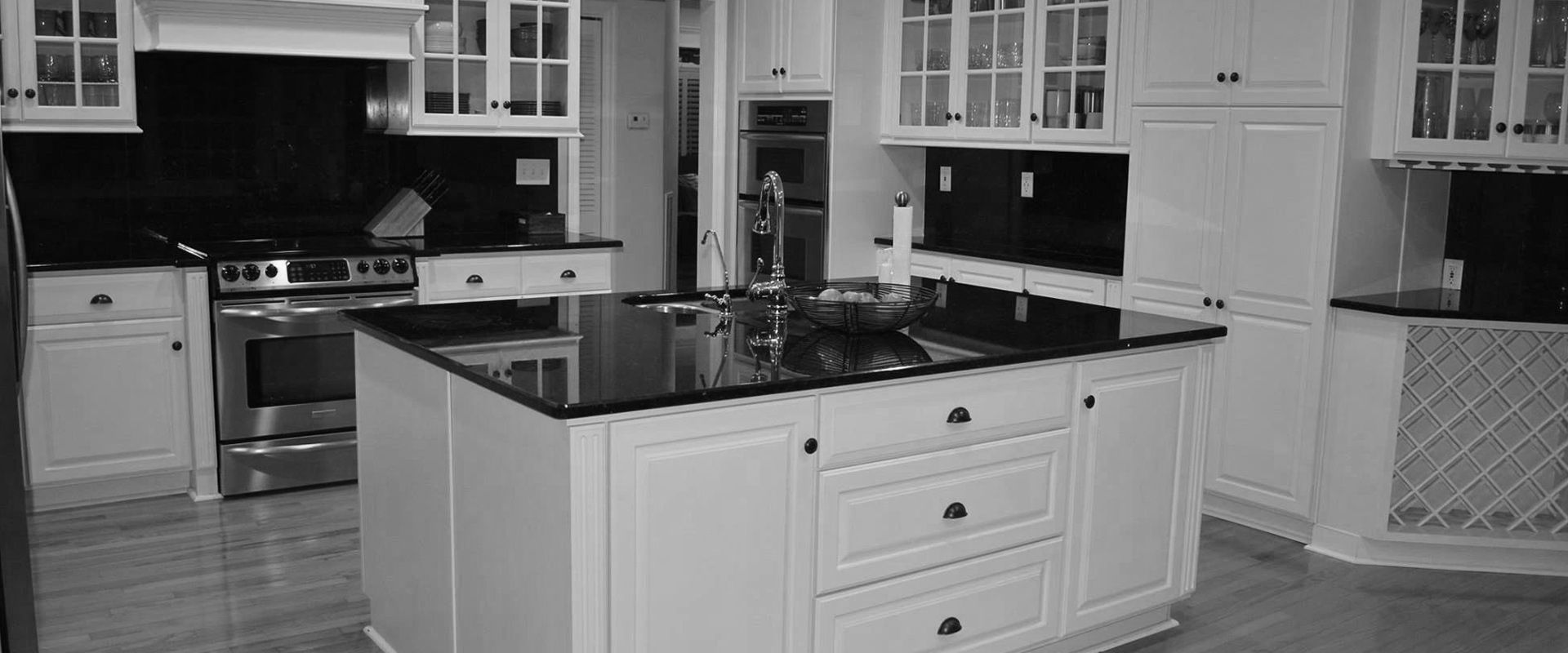 A black and white photo of a kitchen with white cabinets and black counter tops.