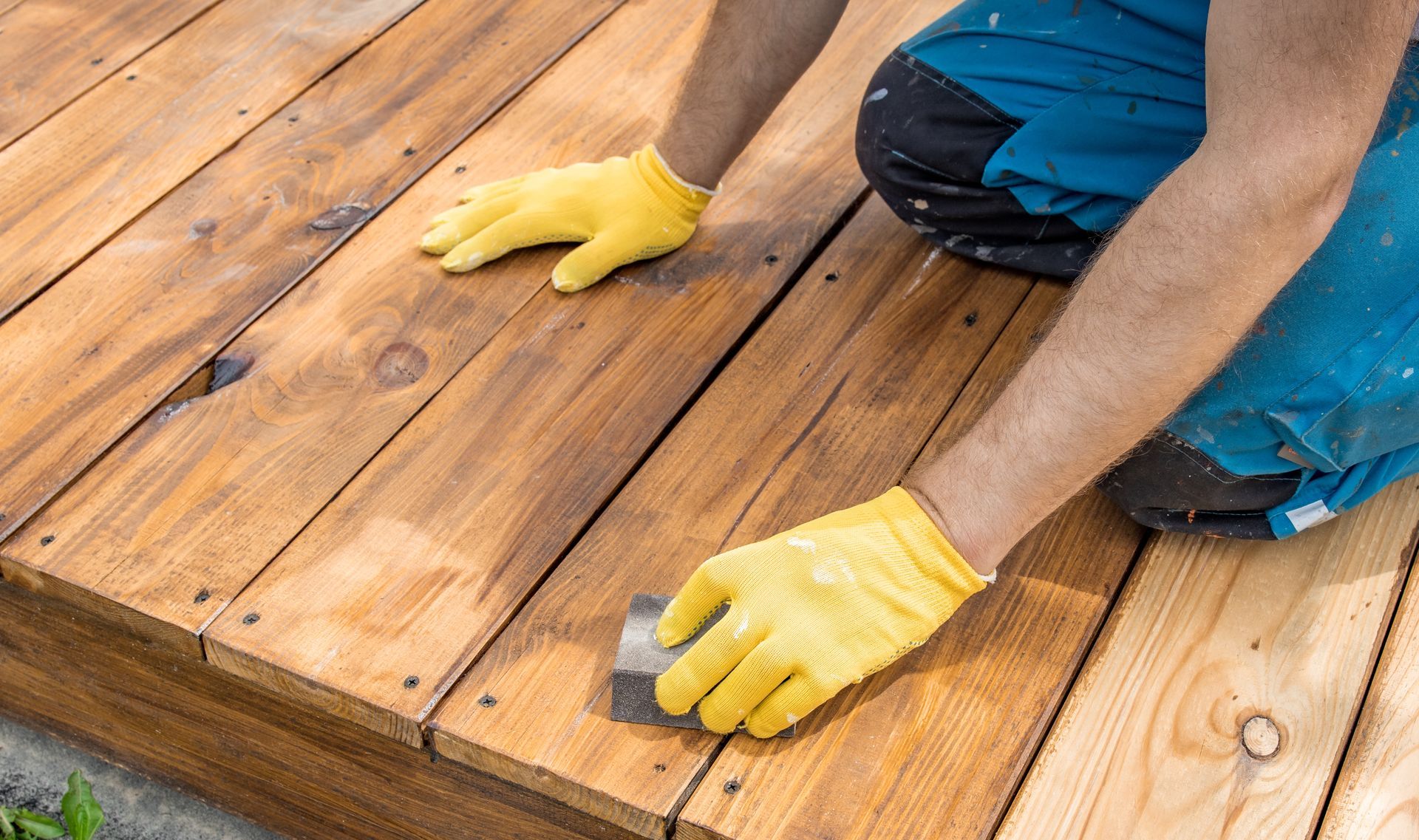 Person in yellow gloves installing wooden deck boards with a drill outdoors