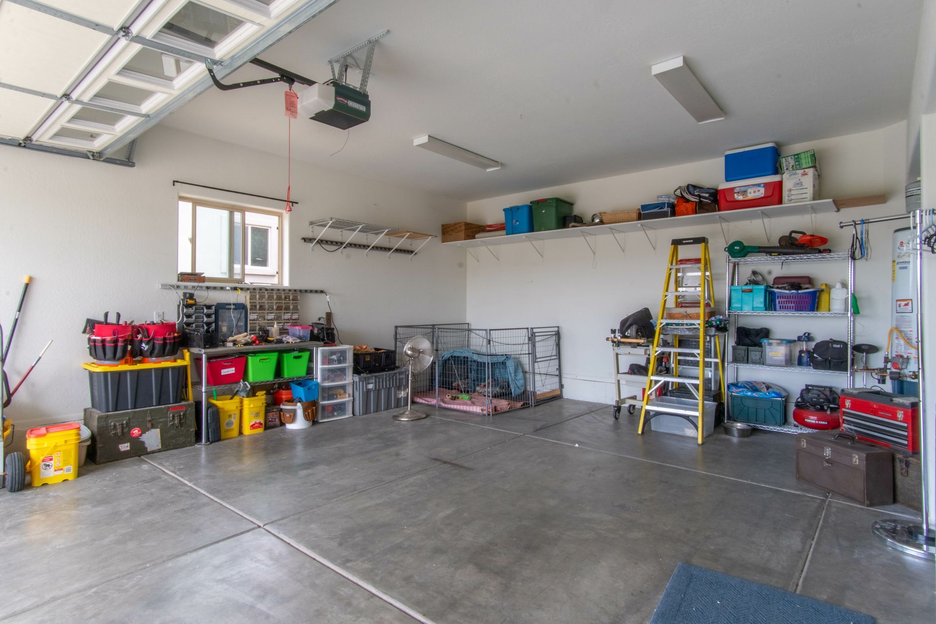 Spacious garage with shelves, tools, bins, a ladder, and a car parked inside.