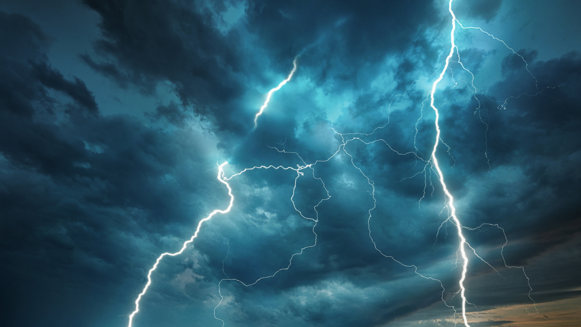 Lightning strikes across dark, stormy, blue-gray clouds.