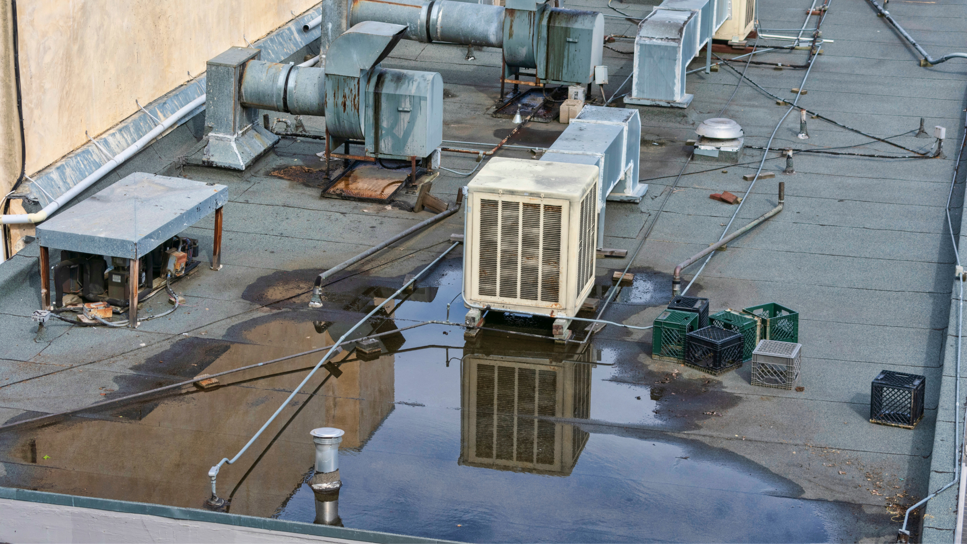 A flat commercial rooftop with various HVAC units, some metal ductwork, and standing water.