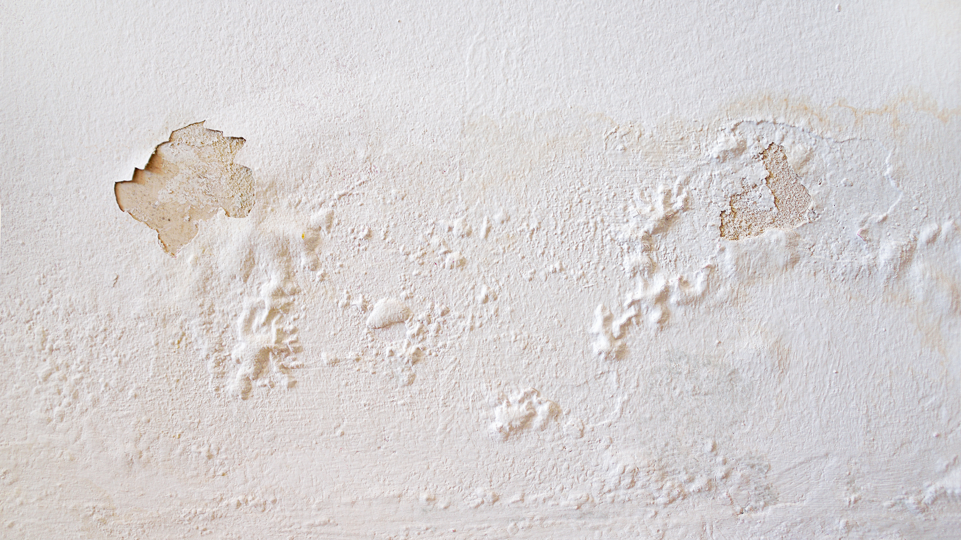 Damaged white wall showing bubbling, flaking paint and discoloration from moisture.