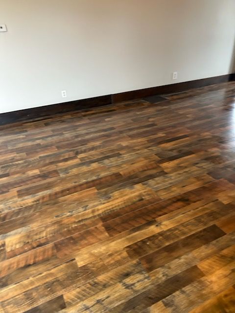 An empty room with light grey walls, a white ceiling fan, and dark wood-look plank flooring. Two windows are visible.
