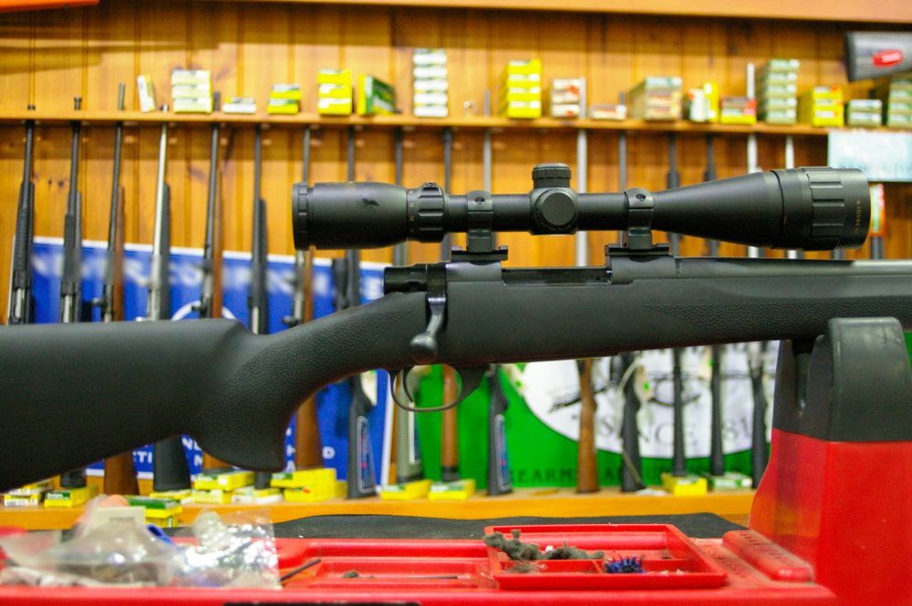 A Black Rifle With a Mounted Scope is Displayed on a Red Rack in a Gun Shop — Mackay Shooters Supplies in Proserpine, QLD