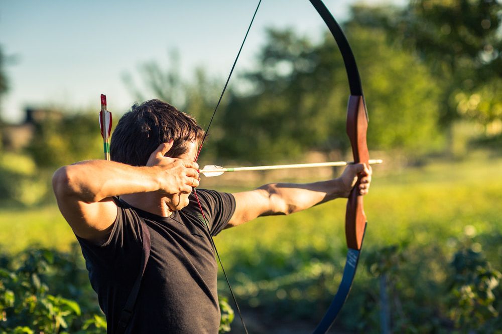 Man Focusing Intensely While Aiming a Bow and Arrow Outdoors in a Lush — Mackay Shooters Supplies in Mount Isa, QLD