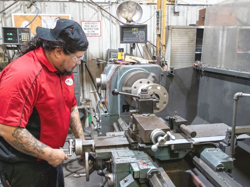 Technician in red shirt operating a lathe in an industrial workshop