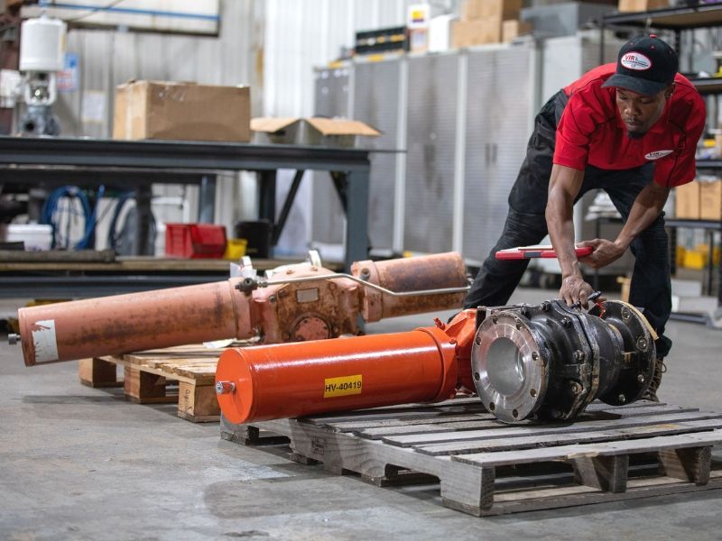 Worker in red shirt inspecting orange industrial cylinders on pallets in a warehouse
