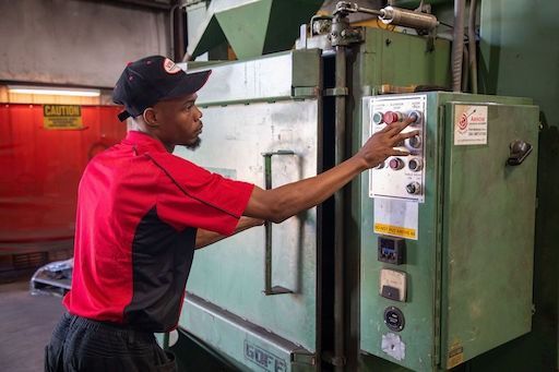 Person in a red shirt and black cap reaches for parts on a warehouse shelf.