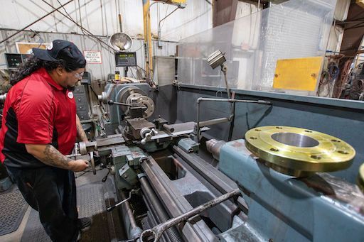 Worker operating a lathe in an industrial machine shop with metal parts and tools nearby