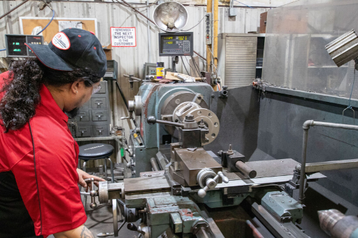 Person in red jacket working on a metal lathe in a machine shop