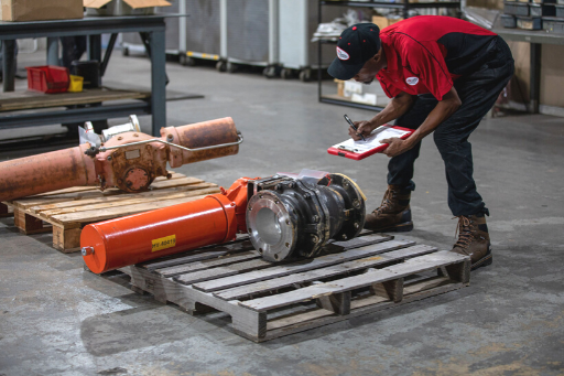 Worker in red shirt inspecting metal parts on pallets in an industrial warehouse