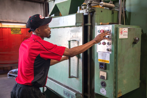 Worker in red shirt operating controls on a large green industrial machine.