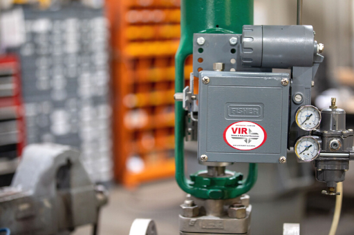 Gray industrial control box with gauges and green piping in a factory setting
