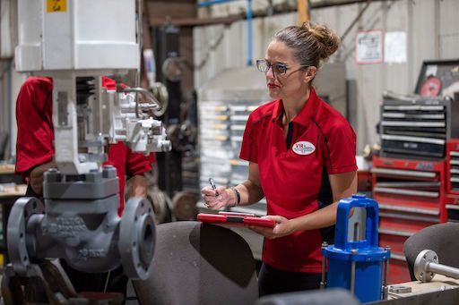 Worker in red shirt writing on clipboard beside industrial machinery in a factory workshop