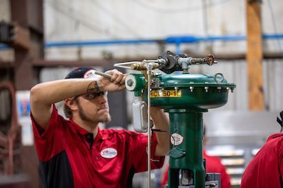 Worker in a red shirt adjusts a green industrial machine in a workshop