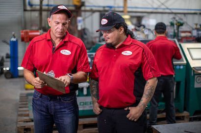 Two workers in red shirts reviewing a clipboard in a factory workshop