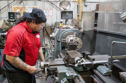 Worker in red shirt operating a metal lathe in an industrial workshop