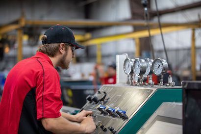 Technician in red shirt adjusting controls on industrial machinery in a factory setting