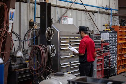 Worker in red shirt using a tool chest in an industrial workshop with hanging cables and parts racks