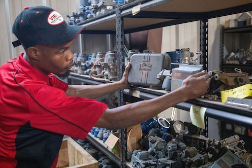 Person in a red shirt and black cap reaches for parts on a warehouse shelf.