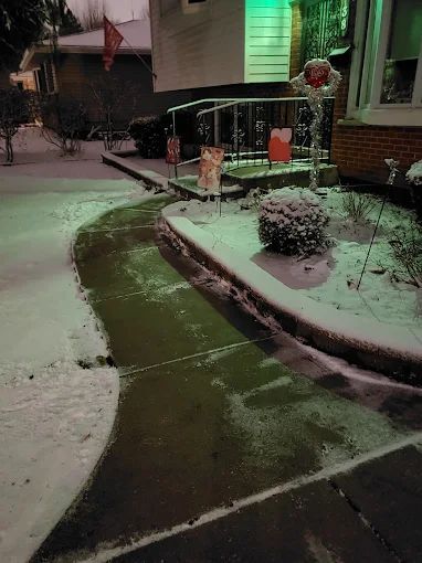 A snowy sidewalk in front of a house at night.