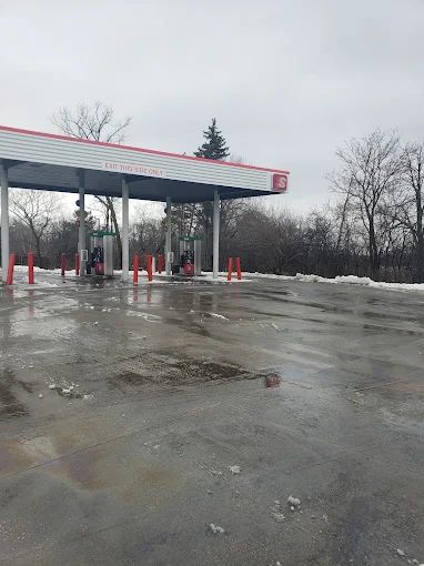 A gas station with a lot of snow on the ground and trees in the background.