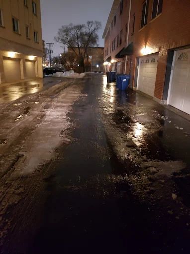 A dark alleyway with a lot of snow on the ground and a building in the background.
