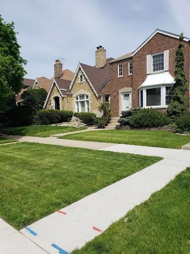 A row of houses with a lush green lawn and a sidewalk in front of them.