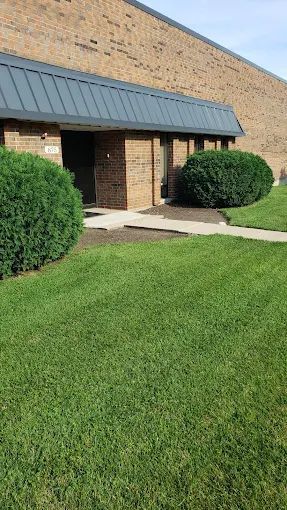 A brick building with a metal roof and a lush green lawn in front of it.