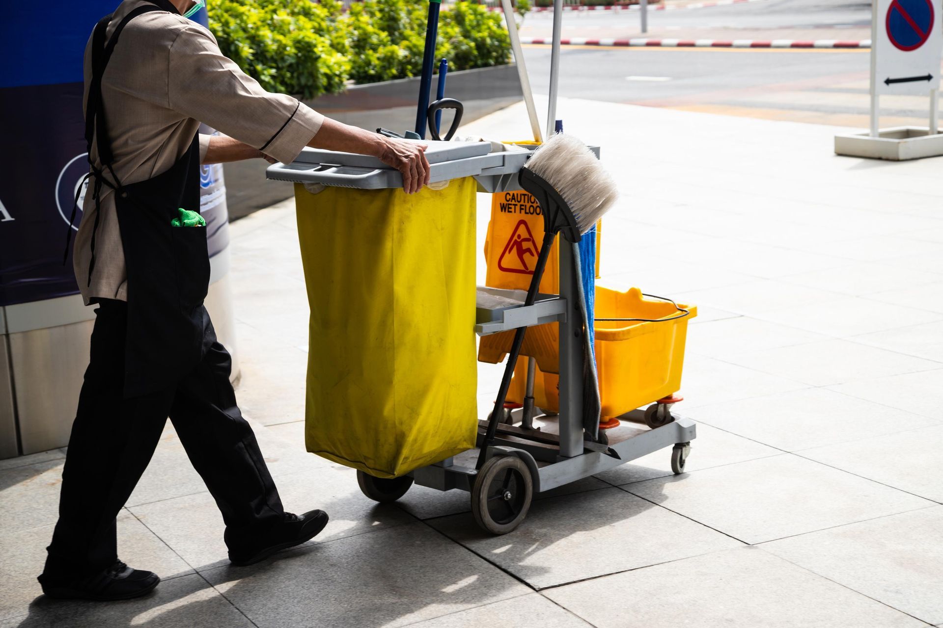 A man is pushing a cleaning cart on a sidewalk.