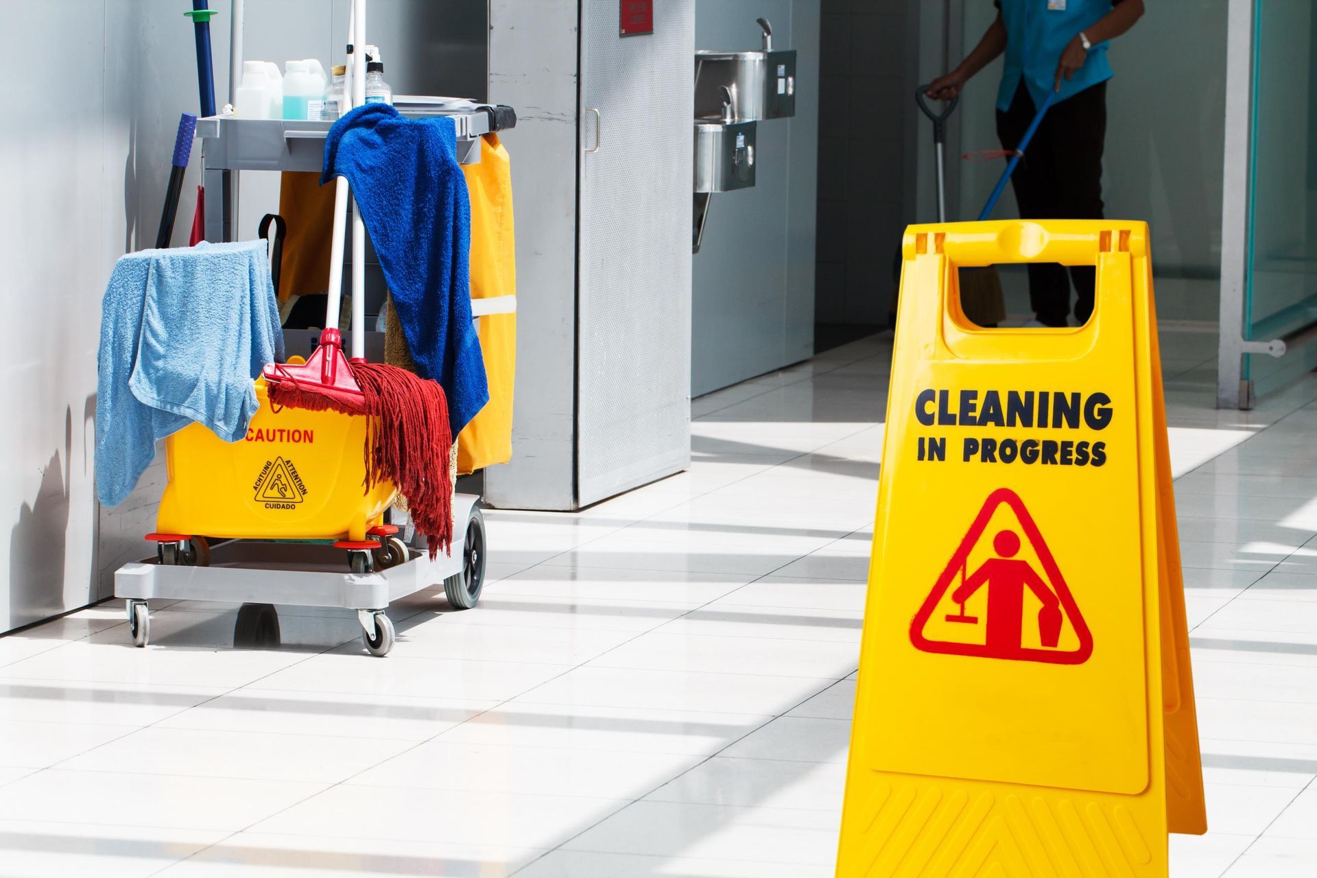 A man is mopping the floor next to a sign that says cleaning in progress