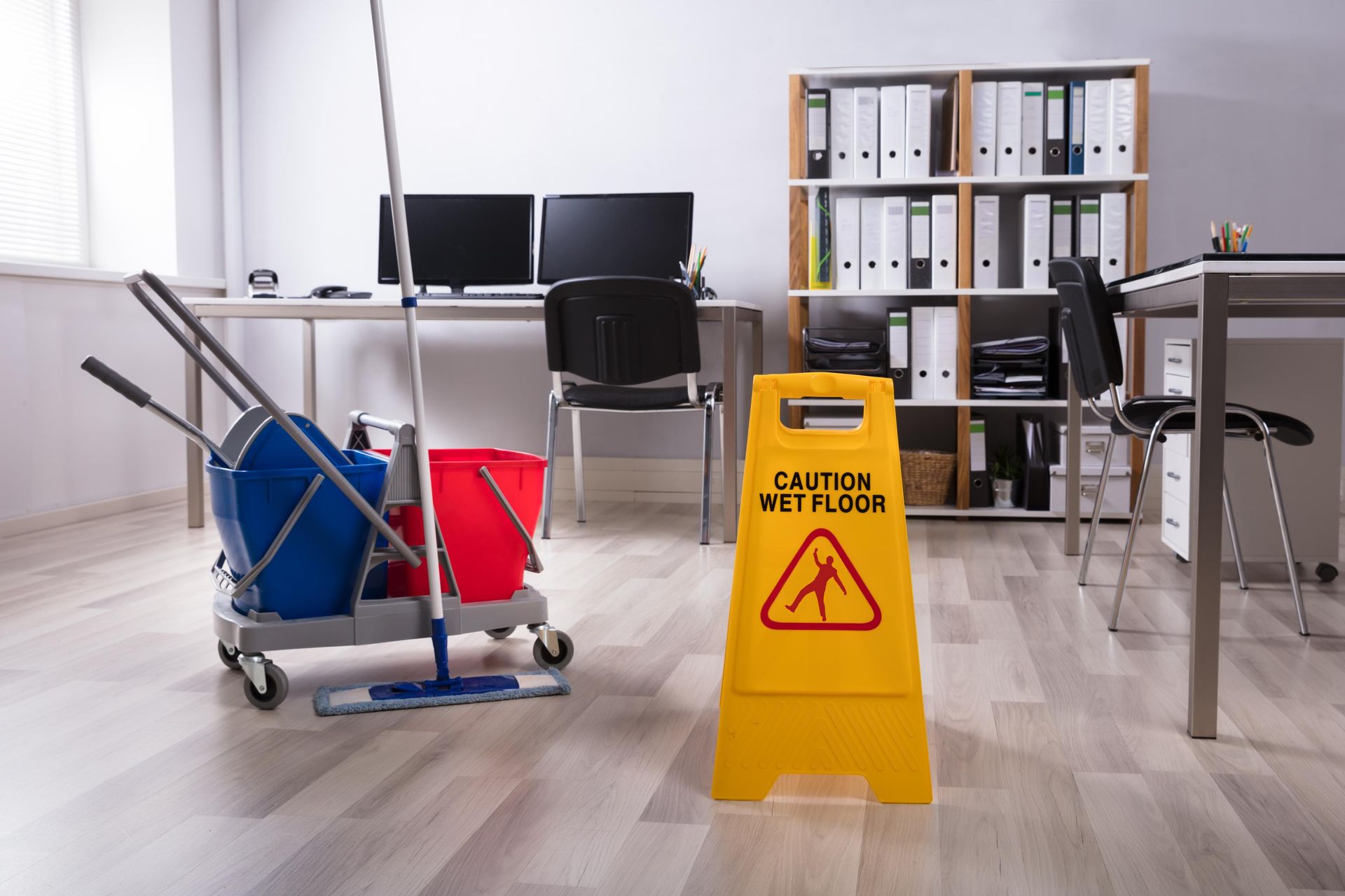 A yellow caution sign is in an office next to a mop and buckets.