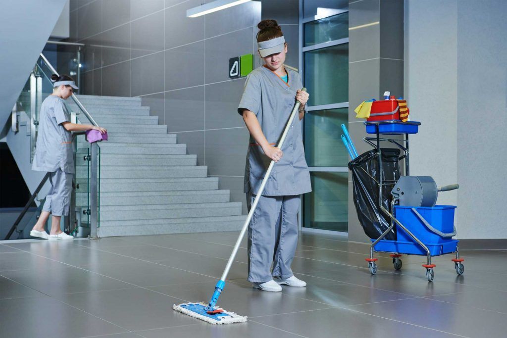 A woman is cleaning the floor with a mop in an office building.