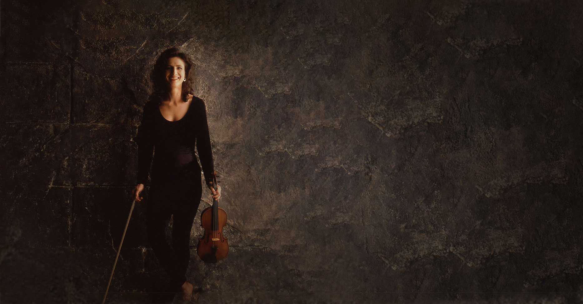 madeleine mitchell against a stone wall background and holding a violin