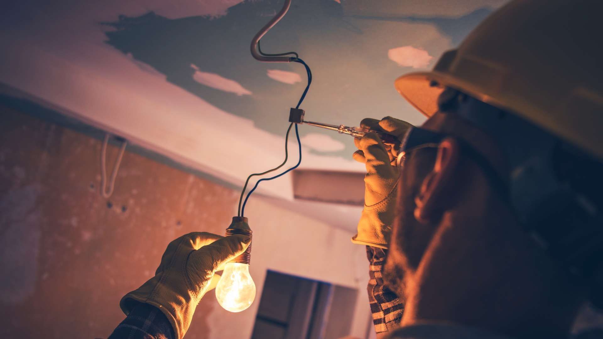 A man is holding a light bulb while working on a ceiling.