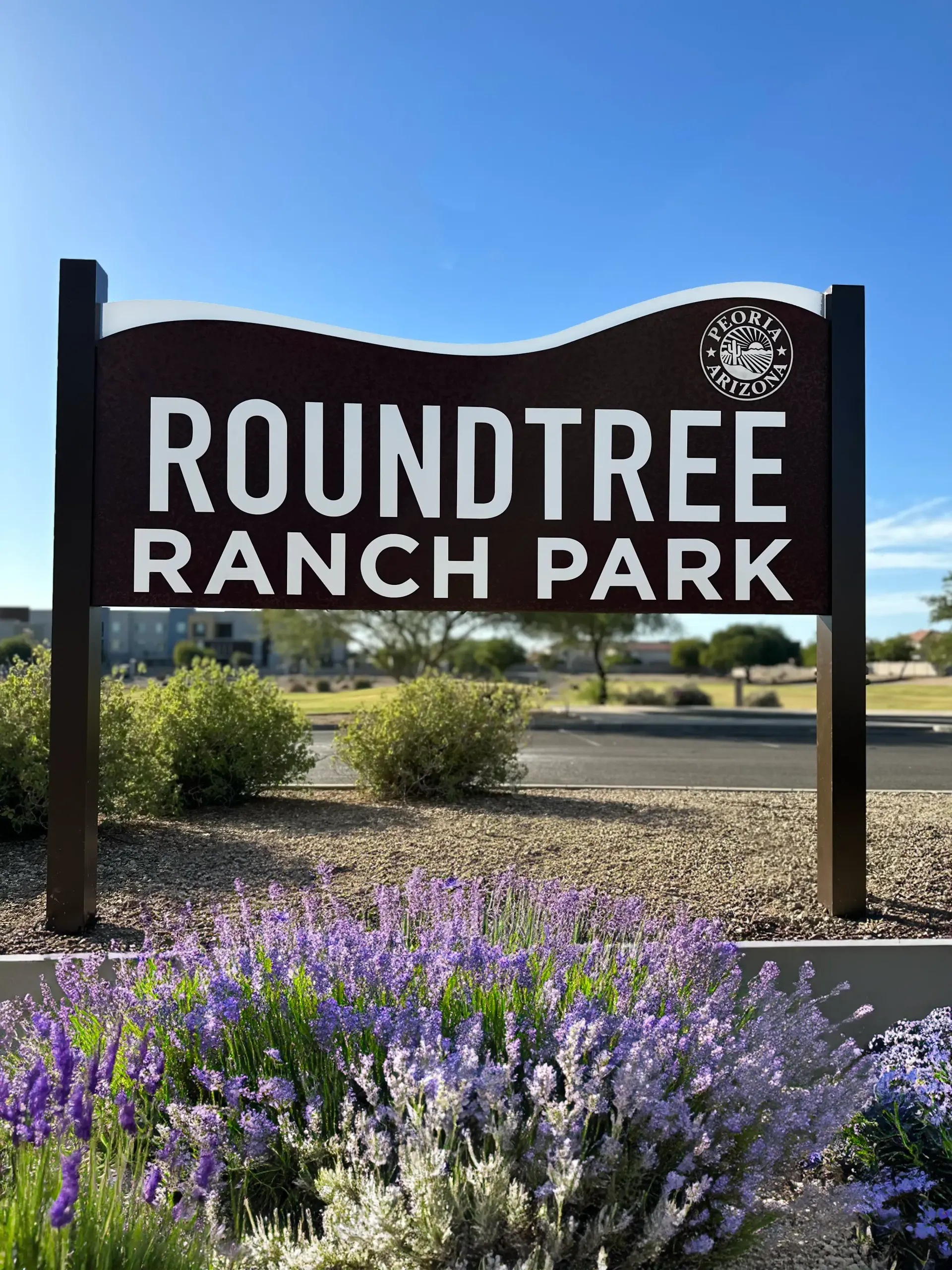 A sign for roundtree ranch park is surrounded by purple flowers.