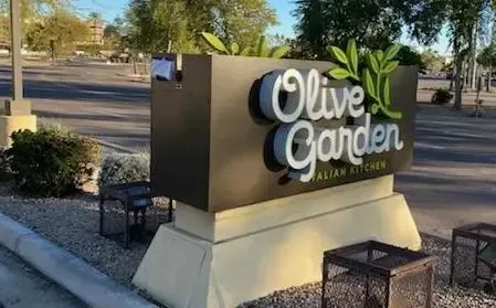 A large sign for olive garden italian kitchen is sitting in a parking lot.