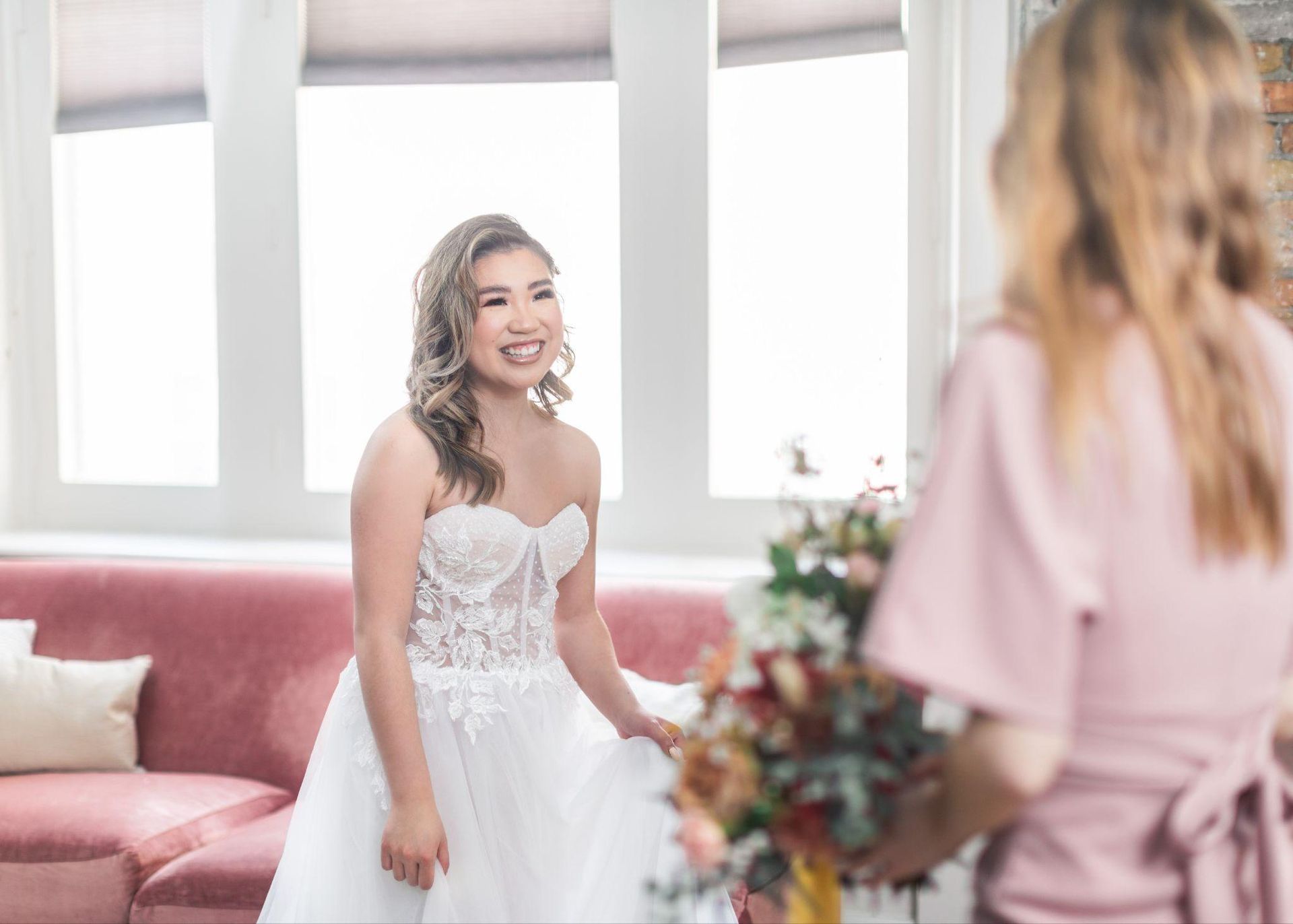 A bride and her bridesmaid are standing next to each other in a living room.